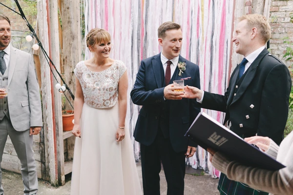 Bride and groom smiling and listening to the officiant in the ribbon-decorated courtyard