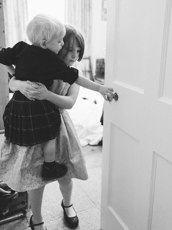 Young woman in white dress holds a little girl in a bright hallway, smiling at the door
