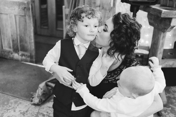 Mother gives a kiss to the little boy during the ceremony — little sister playing around them