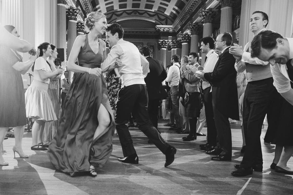 Joyful couple at the centre of the elegant ballroom, guests watching — black-and-white