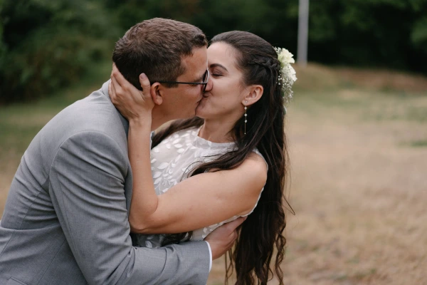 Bride and groom kissing with joyful expression at outdoor wedding with green natural background.