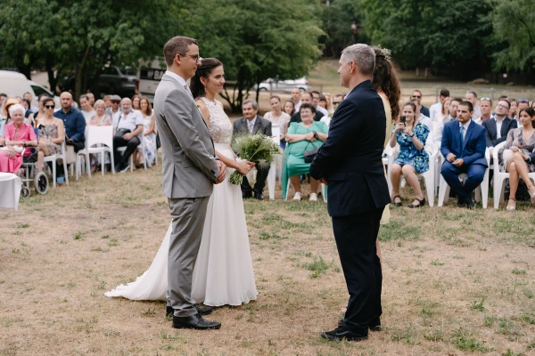 Bride and groom exchanging vows with officiant at outdoor garden wedding ceremony surrounded by guests.