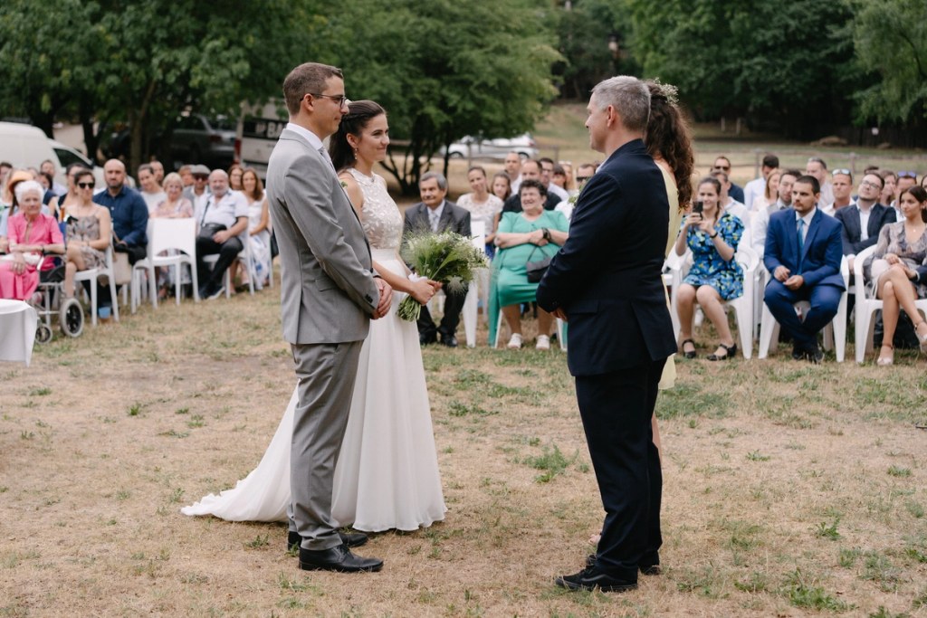Bride and groom exchanging vows with officiant at outdoor garden wedding ceremony surrounded by guests.