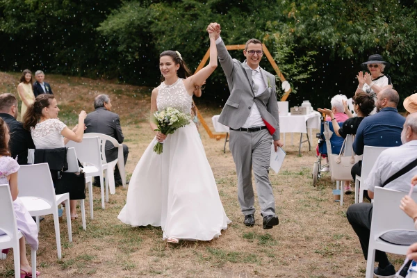Bride and groom raising hands in celebration walking through wedding ceremony guests cheering.