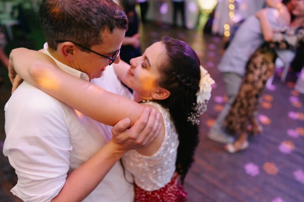 Couple dancing joyfully at wedding reception — colorful ambient lighting, intimate embrace, festive party moment.