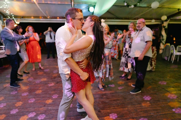 Couple kissing on dance floor during wedding celebration — warm ambient lighting, intimate romantic moment, festive reception backdrop.