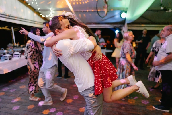 Man and woman dancing with joyful expressions at wedding — colorful purple and gold tent lighting, animated celebration moment.