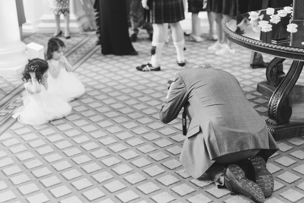 Groom crouches toward the little flower girl at the elegant reception — white flower table behind