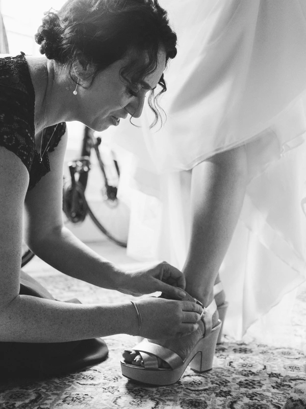 Bride lifts her white lace dress trying to put on her shoes — intimate black-and-white moment