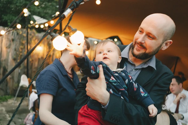 Father and mother hold a small child at the reception, the child points up at the warm light