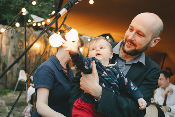 Father and mother hold a small child at the reception, the child points up at the warm light