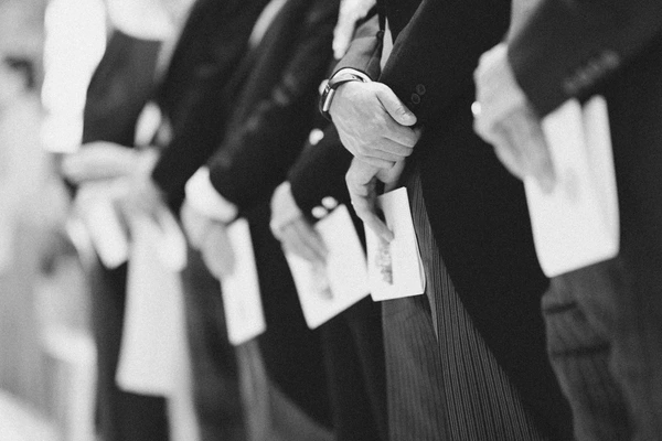 Bride and groom's hands holding the wedding rings — black-and-white detail, formal attire
