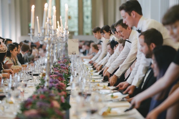 Long wedding dinner table with silver candelabra and pink flowers, guests in white and beige