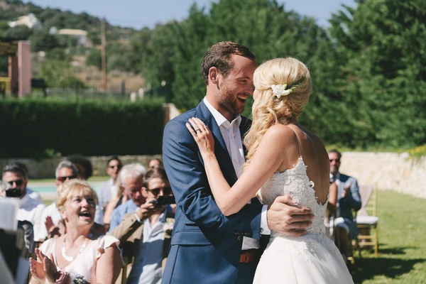 Bride and groom laughing at each other at the ceremony — guests seated in the green garden