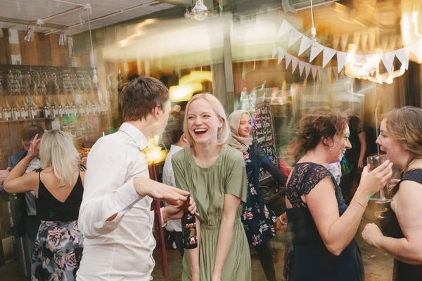 Guests enjoy a lively party — woman in green laughing and dancing, friends with glasses in hand