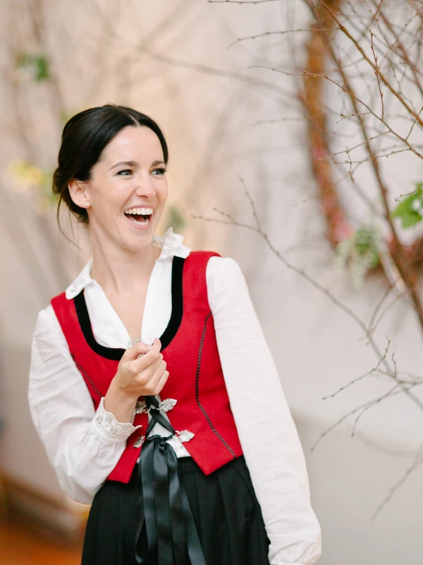 A woman in a floral dress dances with arms raised on the crowded wedding dance floor surrounded by other guests. Candid documentary wedding photograph.