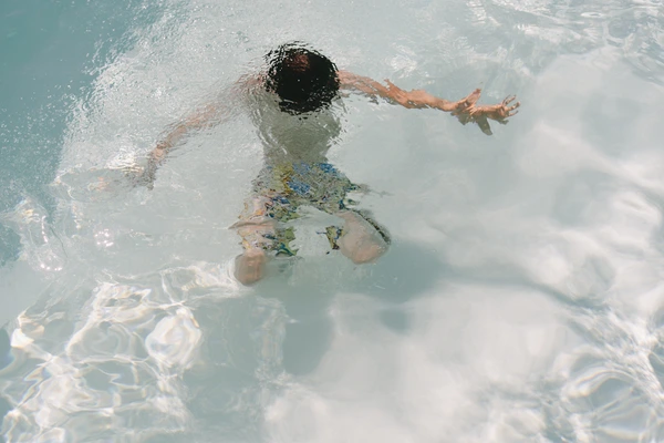 Child swimming in crystal-clear sea, splashing water, colourful swimwear, sunny summer day