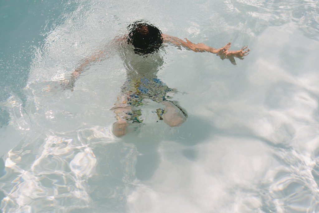 Child swimming in crystal-clear sea, splashing water, colourful swimwear, sunny summer day