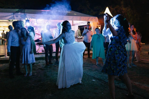 Wedding guests dancing outdoors at night celebration with bonfire and atmospheric lighting.