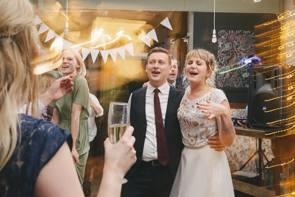 Bride and groom chat cheerfully with guests amid warm white light decoration and bunting flags