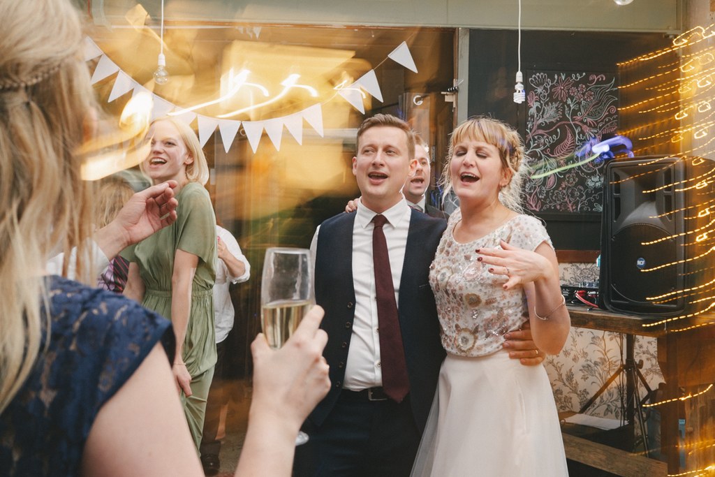Bride and groom chat cheerfully with guests amid warm white light decoration and bunting flags
