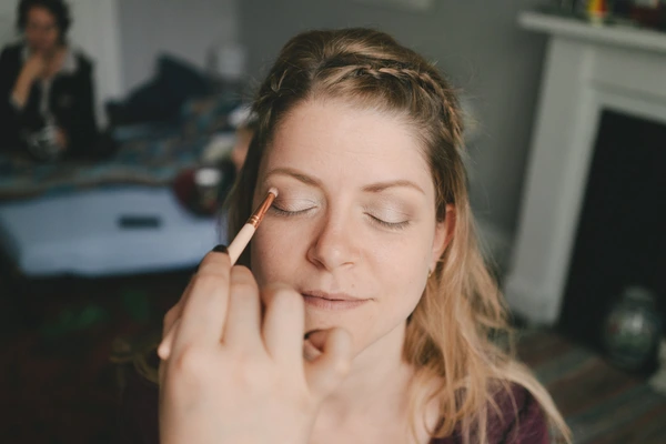 Makeup artist applies eyeshadow to the bride — closed eyes, natural light