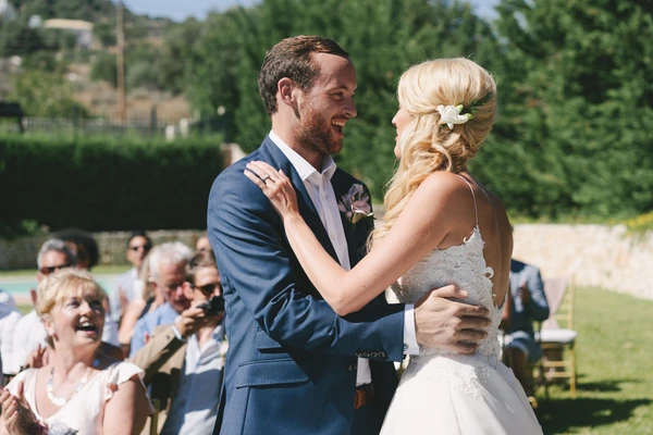 Groom and bride in white lace laughing and looking at each other — guests applauding in sunny garden
