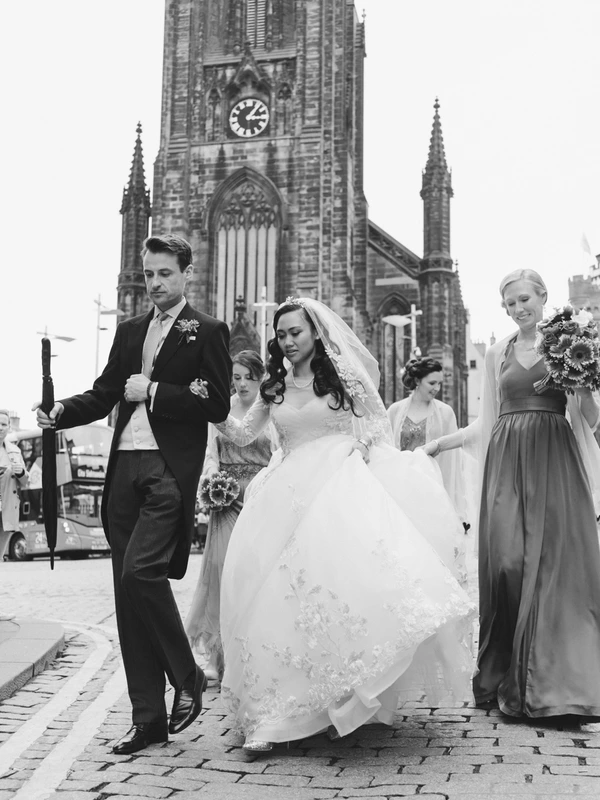 Bride and groom in front of a Gothic church, attendants with bouquets beside them