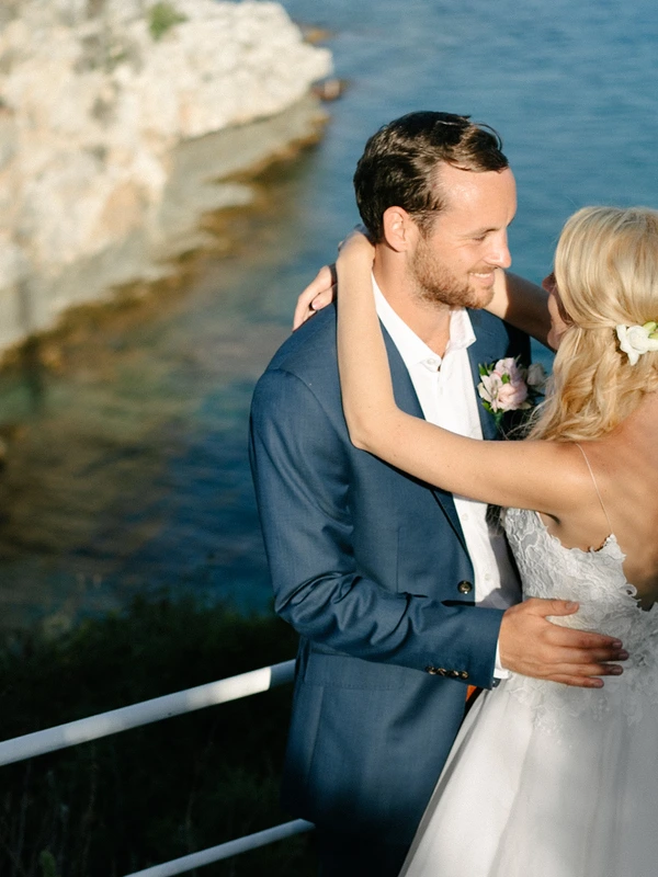 Bride hugs groom by seaside rocks — genuine joy and love on both faces