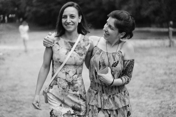 Black and white photo of two women walking arm in arm at outdoor wedding reception.