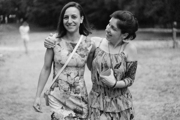 Black and white photo of two women walking arm in arm at outdoor wedding reception.