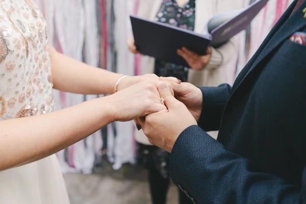 Groom places ring on bride's finger during the ceremony, bride in ornately embroidered dress