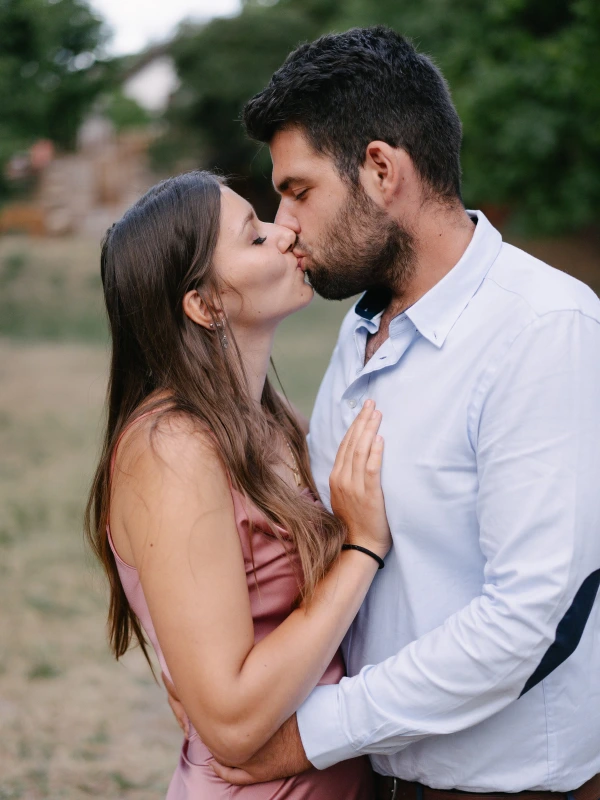 Couple kissing passionately at outdoor wedding with green field and natural venue background.