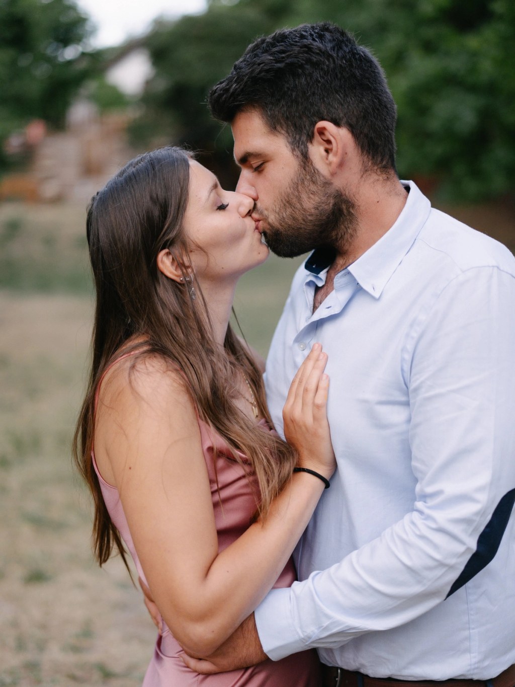 Couple kissing passionately at outdoor wedding with green field and natural venue background.