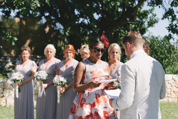 Wedding ceremony under an old tree — groom in white suit talks to bride in floral red-white dress