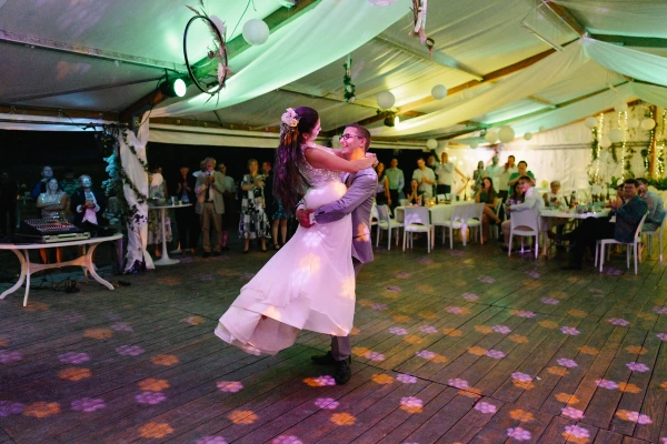 Bride and groom dancing at evening wedding reception with guests watching under tent lights.