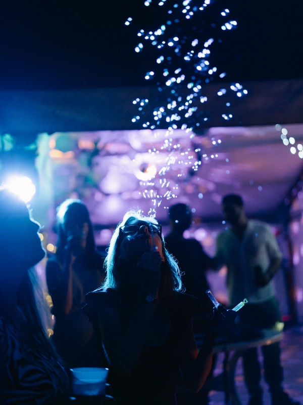 Wedding guests dancing under decorative lights — evening celebration, colorful ambient lighting, festive dance floor moment.