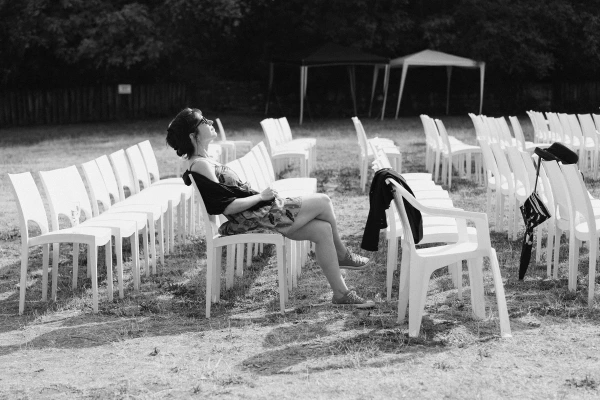 Black and white photo of girl sitting on white chair at wedding venue before ceremony begins. Documentary wedding photography capturing quiet moments.