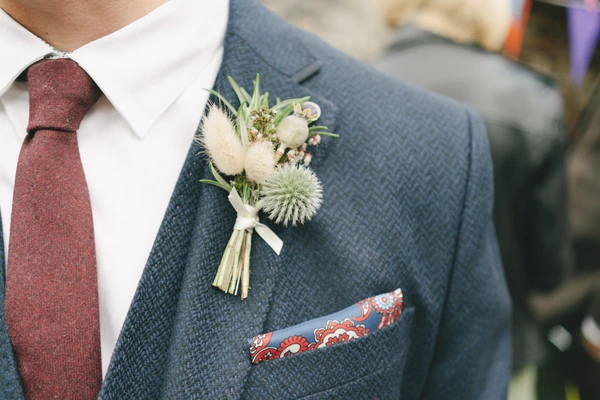 Groom in dark grey suit with burgundy tie — white and green flower buttonhole, pocket square