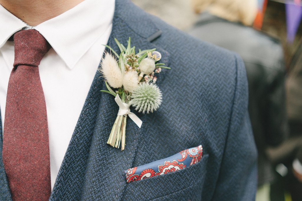 Groom in dark grey suit with burgundy tie — white and green flower buttonhole, pocket square