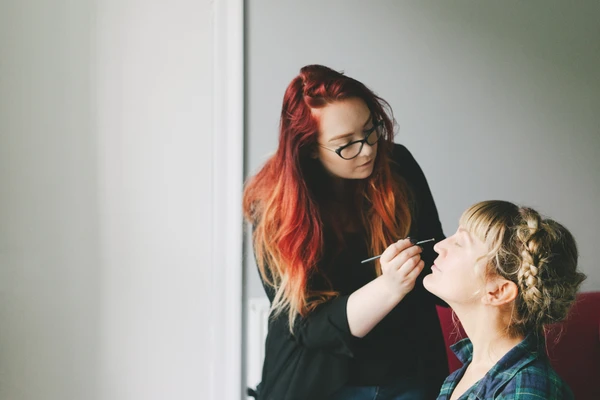 Red-haired makeup artist brushes the beaming bride's face during preparations