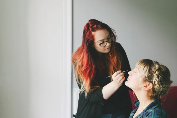 Red-haired makeup artist brushes the beaming bride's face during preparations