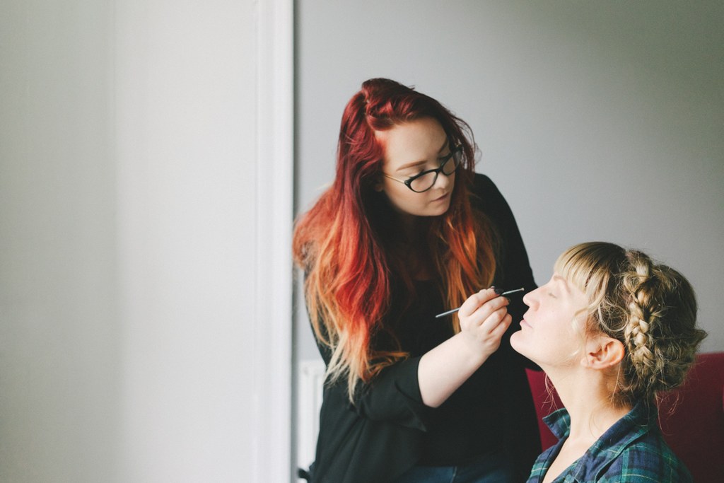 Red-haired makeup artist brushes the beaming bride's face during preparations