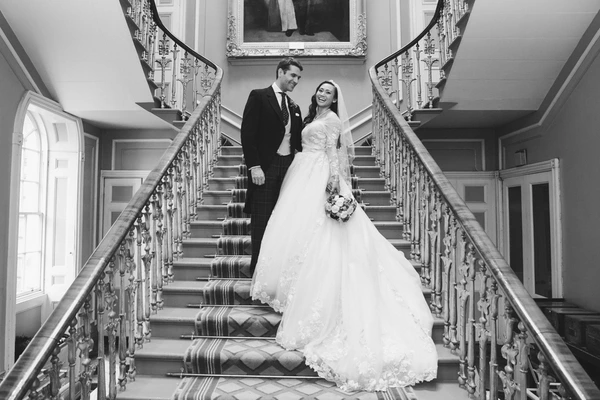 Bride and groom on ornamental stone staircase — bride holds her lace train, smiling at each other