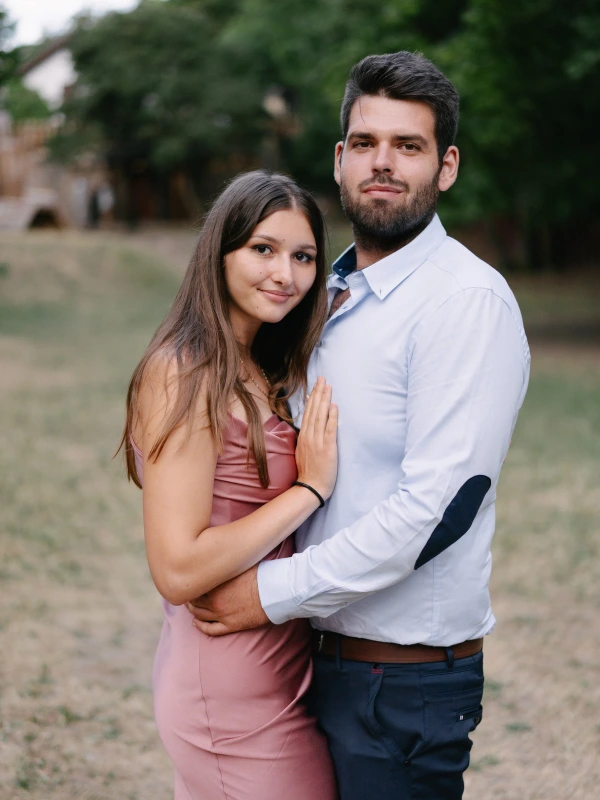 Couple posing together in pink and white outfit at outdoor wedding venue with green background.