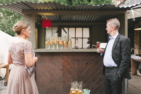 Guests at the bar in the wedding reception — wooden bar, bottles in a row, green corrugated roof