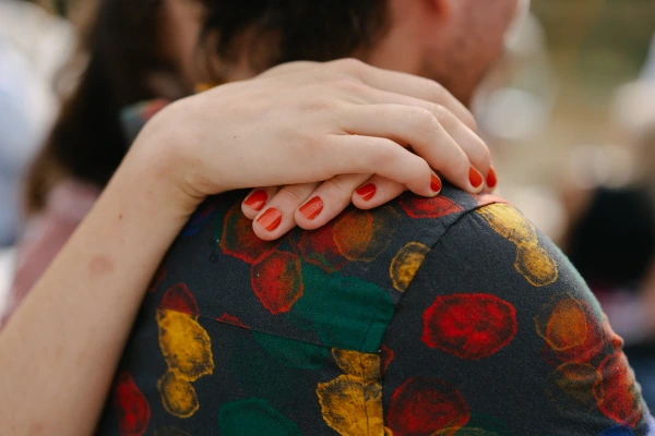 Close-up of woman's hand with red nail polish resting on colorful patterned fabric at wedding.