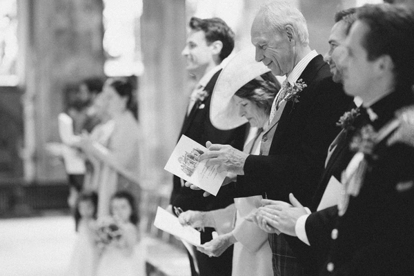 Elderly man and woman at the ceremony holding papers — dark suits, flower buttonhole, church interior