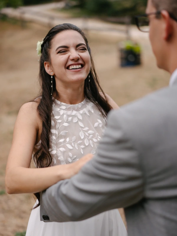Bride smiling and looking at groom during wedding moment at outdoor venue with natural background.