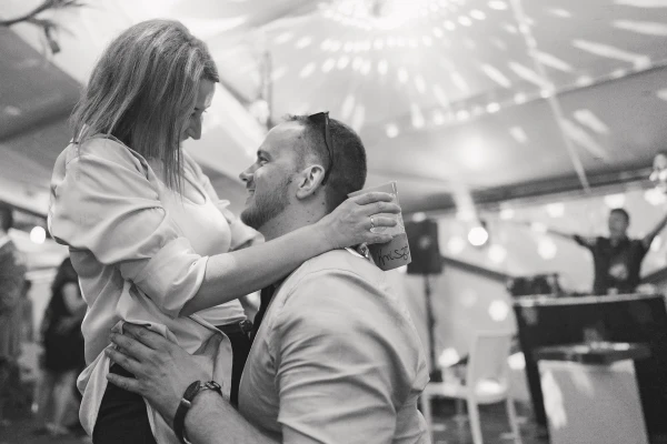 Couple dancing tenderly under tent venue — black and white photography, intimate moment, reception lighting.